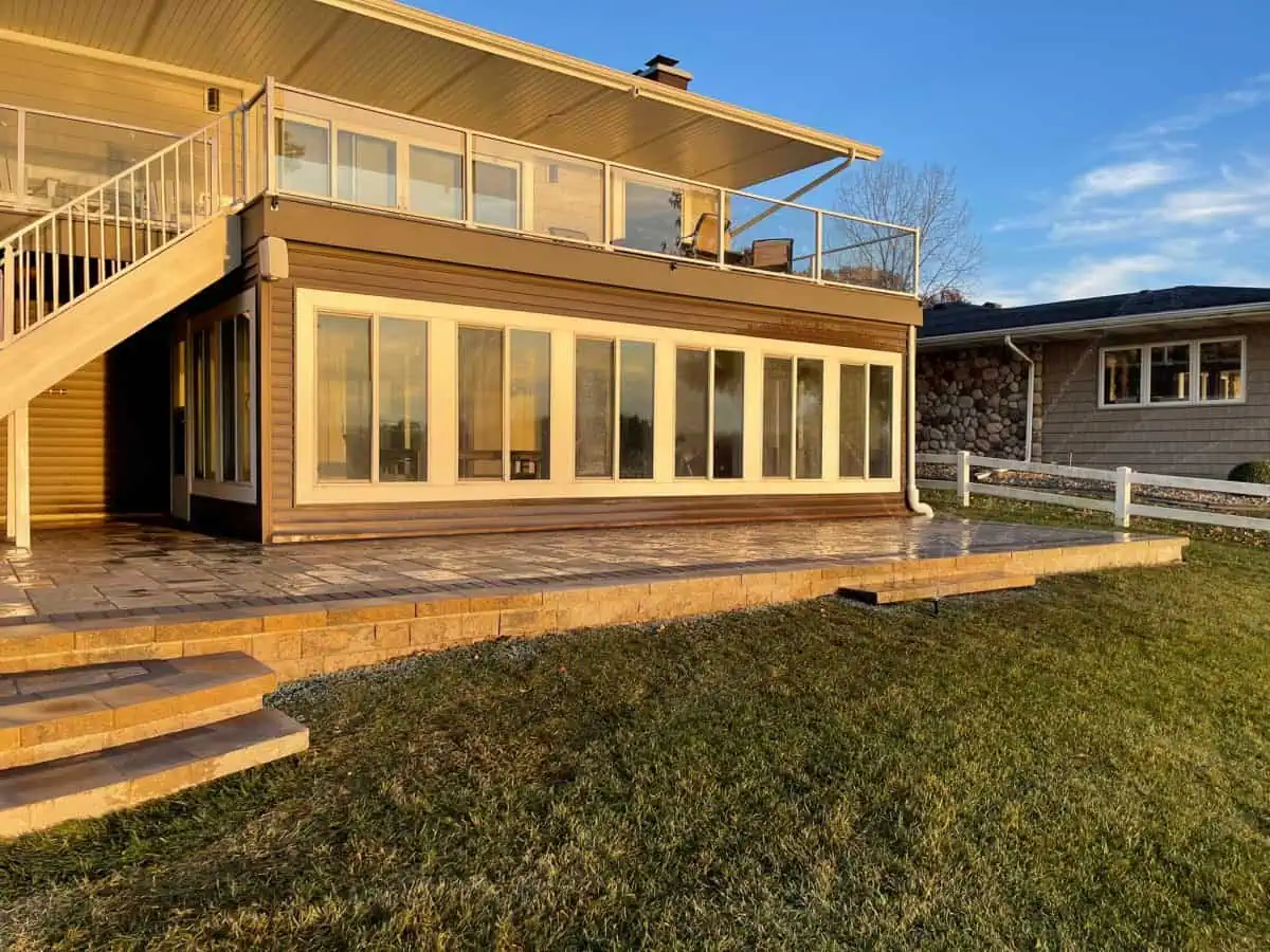Multi-level stamped concrete patio with raised deck, staircase, and large sliding glass doors on a lakefront home in Northwest Indiana, designed and installed by Dean's Pools and Landscaping