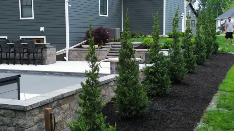Lush greenery and stone features enhance a backyard landscape design in Northwest Indiana, featuring a pool area and seating.